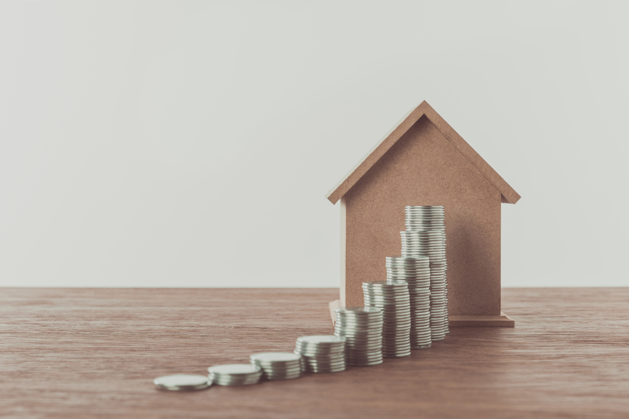 Stacks of coins and small house on brown wooden tabletop, saving concept